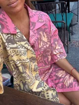 Camisa oversize de manga corta con cuello camisero, confeccionada en tejido de viscosa y lino. Presenta un diseño estampado de estilo patchwork, dividido verticalmente en dos mitades: una en tonos amarillos y marrones, y la otra en tonos rosados y morados.