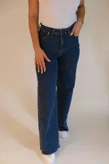 Jean wide leg de tiro alto, color azul oscuro. Tiene dos bolsillos redondeados en la cadera en la parte delantera y dos bolsillos en la parte trasera. Cuenta con botón metálico, cremallera y terminación de ruedo desflecado.