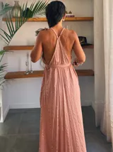Vestido largo blanco con finas rayas verticales en lurex dorado. Presenta un escote profundo en V con tirantes finos que se anudan en la nuca (estilo halter) y un corte imperio con frunces en la cintura.