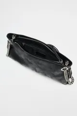 Bolso alargado negro con tachas plateadas en el borde inferior y detalle de cremallera en el corte. Tiene asa de cadena plateada multiposición para usar al hombro o como bandolera. Incluye bolsillo interior con cremallera y cierre principal con cremallera.
