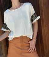 Remera negra de corte holgado con mangas cortas con volados y detalle de apliques de piedras en los volados.