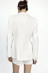 Blazer blanca entallada con cuello solapa combinado, manga larga con hombreras, bolsillos de plastrón en delantero, costuras marcadas, forro interior a tono y cierre frontal con botón forrado.