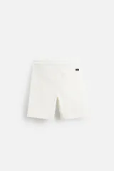 Bermuda color verde militar de corte relajado, confeccionada en tejido de algodón. Tiene cintura elástica ajustable con cordón interior, bolsillos frontales y bolsillo trasero de parche.