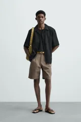 Camisa color marrón oscuro de corte relaxed fit, confeccionada en tejido de lino. Tiene cuello bowling, manga corta, bajo con aberturas laterales y cierre frontal de botonadura.