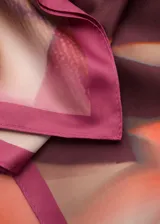 Pañuelo cuadrado con diseño abstracto en tonos rosa, naranja y borgoña, con borde liso en color fucsia.