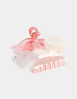 Set de cuatro broches para el pelo de diferentes formas y colores: uno con forma de moño rosa y rojo, uno rectangular color crema, uno transparente y uno con forma de media luna rosa marmolado.