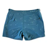 Short de baño azul con estampado de palmeras, pretina fija con hebillas metálicas laterales, botón a presión y cierre frontal. Incluye tres bolsillos (dos laterales y uno trasero). Confeccionado en tela con 10% spandex de secado rápido y mesh hipoalergénico en el interior.
