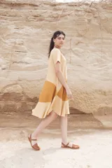 Vestido corto color mostaza con corte evasé y mangas cortas. Presenta un bloque de color marrón en la falda y otro bloque color beige en el ruedo.