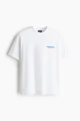 Remera blanca de algodón con cuello redondo y manga corta, corte holgado. Presenta un pequeño estampado en el pecho con el texto "PEANUTS Racing Team" en letras azules y rosadas.