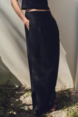 Pantalón negro con bordados florales en los laterales, tiro alto, cintura elástica en la parte trasera, bolsillos laterales, pliegues y cierre frontal con cremallera, botón interior y gancho metálico.