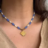 Collar corto con cuentas de cristal facetado color azul, cuentas cilíndricas blancas y detalles dorados. Dije de San Benito dorado.