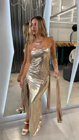 Vestido largo dorado metalizado, strapless, con drapeado lateral y abertura en la pierna. Incluye lazo lateral.