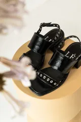 Sandalias negras de charol con tacón cuadrado y detalles de remaches metálicos.