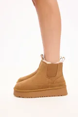 Bota tipo chelsea color camel, confeccionada en gamuza con interior forrado en piel sintética. Presenta elásticos laterales, tirador en la parte trasera y plataforma alta con suela dentada.
