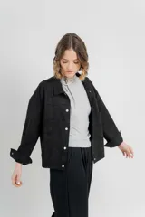 Chaqueta negra corte camisa de gamuza con elastano, de corte recto y abotonada en el frente con botones metálicos. Presenta bolsillos grandes en el frente.