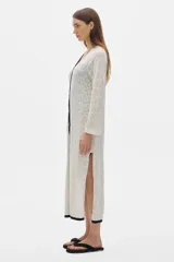 Túnica tipo vestido tejido calado color blanco, con cuello en V y ribete negro, abotonada adelante, de largo midi y con cortes a los lados.