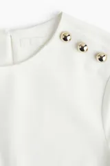 Vestido corto blanco de corte evasé, con cuello redondo y manga corta. Presenta abertura de cerradura con botón oculto en la nuca.
