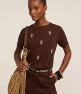 Blusa marrón de mangas cortas, confeccionada en viscosa, con cuello redondo y bordados de piñas en la parte delantera.