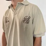 Chomba azul de piqué con cuello clásico y manga corta. Presenta bordados blancos con motivos de golf en el pecho.