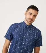 Camisa de manga corta azul con estampado de círculos blancos, cuello camisero, abotonada al frente y con bolsillo en el pecho.