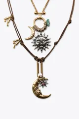 Set de dos collares de diferentes largos. El primero es una cadena dorada de eslabones con dije circular y charms colgantes. El segundo es un collar de cordón marrón con nudos y dijes metálicos de sol y luna.