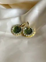 Par de aros colgantes con forma circular, de resina color verde con glitter, borde dorado con strass y arito de acero quirúrgico.