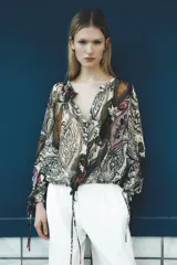 Blusa semitransparente de cuello redondo y manga larga con lazadas ajustables en los puños. Tiene bajo ajustable con lazada y cierre frontal con botones ocultos.