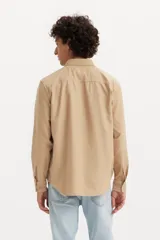 Camisa de manga larga color beige, con cuello abotonado y cierre frontal con botones.