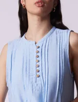 Vestido blanco de algodón y rayón, marca Dash. Cuello a la base, sin mangas y abertura central con botones. Delantera con detalle plisado y laterales con bolsillos.