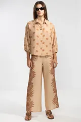 Camisa color beige con estampado de flores y rayas verticales marrones, de manga larga con puños elastizados y lazos regulables en los costados del ruedo.