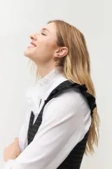 Chaleco blanco con finas rayas verticales negras, escote en V, cierre frontal con botones negros y volados en lino negro en los hombros. La parte inferior presenta otro volado en la misma tela del cuerpo.