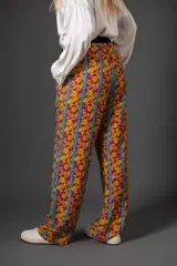 Pantalón de viscosa con estampado floral en tonos fucsia y amarillo, con rayas verticales turquesas. Presenta cintura elastizada con detalle de terciopelo violeta y lazo con borlas.