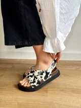 Sandalias con estampado de vaca en blanco y negro, con plataforma marrón y suela negra.