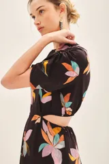 Vestido corto negro con estampado floral abstracto en tonos pastel (rosado, naranja, celeste, amarillo). Presenta cuello redondo, mangas cortas abullonadas y abertura horizontal en la cintura.