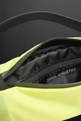 Riñonera deportiva color amarillo flúor, con cierre de cremallera termosellada, bolsillo interno con cremallera y doble mosquetón. Cuenta con banda elástica frontal y asa ajustable con hebilla de liberación rápida.