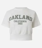 Blusa cropped de algodón color blanco, con cuello redondo, manga corta y estampa lettering "Oakland California 1995" en el frente.