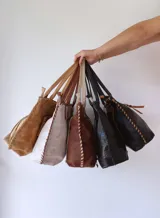 Bolso tipo tote de cuero color camel, con costuras a la vista y tiras de ajuste laterales.