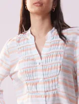 Blusa estampada a rayas horizontales en tonos celeste, blanco y naranja, con cuello mao, escote en V y abertura con botones. Delantero con punto smock. Manga ¾ con terminación amplia.