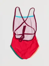 Traje de baño entero rojo con tirantes finos y espalda cruzada. Presenta un parche bordado con un monstruo en la parte inferior. Tiene ribetes en color borgoña y celeste en la parte superior, y ribetes en color naranja y verde en la parte inferior.