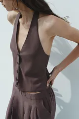 Chaleco marrón con cuello halter ajustable con lazada y escote pico. Cierre frontal con botones.