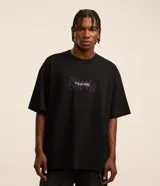 Remera negra de corte oversized, confeccionada en tejido de malla de algodón sostenible. Presenta cuello redondo, mangas cortas y estampa tribal con lettering en el frente.