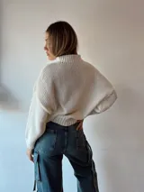 Sweater de punto color crema con cuello alto y estampado de dos peces azules en el frente.