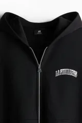 Campera negra con capucha, cierre frontal y bolsillos laterales. Estampado blanco con texto en el pecho.