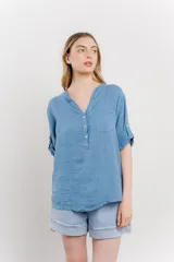 Camisa azul de lino con escote en V abotonado, bolsillo frontal y mangas 3/4 con trabilla.
