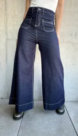 Pantalón de jean azul oscuro, de corte ancho, con bolsillos delanteros cuadrados y costuras blancas contrastantes.