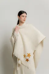 Ruana color crema de tejido grueso con flecos y apliques de estrellas doradas.