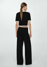 Pantalón negro de punto fino con diseño recto y largo, tiro medio, cintura elástica, ribetes en contraste y bolsillos de ribete delanteros con botones decorativos.