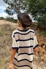 Vestido tejido artesanalmente en hilado 70% algodón y 30% acrílico, con cuello redondo y mangas cortas. Diseño a rayas horizontales en tonos crudo, naranja y beige. Corte recto con aberturas laterales en el ruedo.