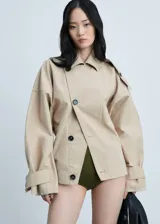 Abrigo color beige con cierre delantero con botones cruzados, cuello camisero, manga larga con trabillas, diseño corto y recto, dos bolsillos laterales y forro interior.