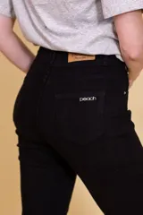 Pantalón jean negro de tiro alto, con cinco bolsillos, confeccionado en tela con elastano. Tiene cierre frontal con doble botón y cierre metálico, y detalle de cuero en la parte delantera de la pretina.